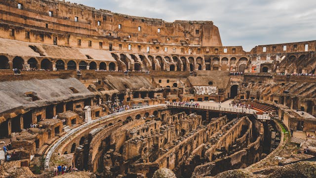 Interior of the Colosseum in Rome showing the hypogeum and arena, with tourists exploring the ancient Roman amphitheater.